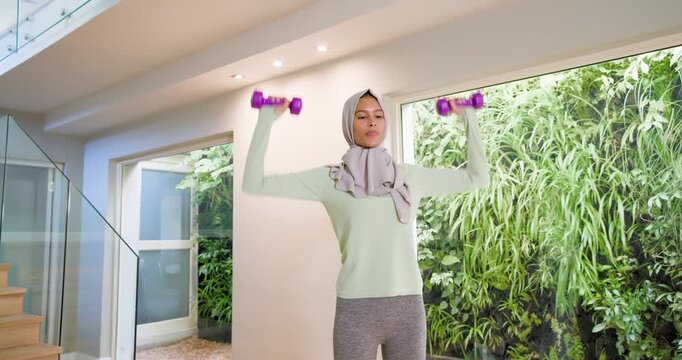 Woman with scarf holding shoulder purple weights pressing side raises at home by window for workout