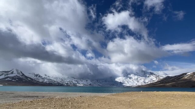 Dramatic timelapse showing a thick sea of clouds flowing over rugged snow-capped peaks and settling above a vast Tibetan sacred lake at high altitude.
