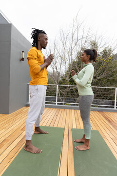 Man and woman practicing yoga on rooftop with cable railing and outdoor light on green mats