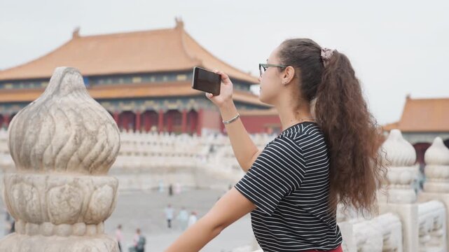 Black woman traveler forbidden city balcony, curly hair and glasses, smartphone selfie capturing ornate stone balustrade and distant palace roofs, overcast sky, contemplative history student
