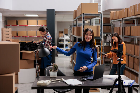 Asian woman streaming warehouse workers team managing dispatching for social media channel. Retail startup business storehouse worker filming explainer video on smartphone of inventory management
