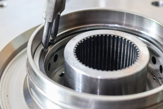 Close-up of mechanic using snap ring pliers to install internal circlip on metal gear shaft in automotive workshop.