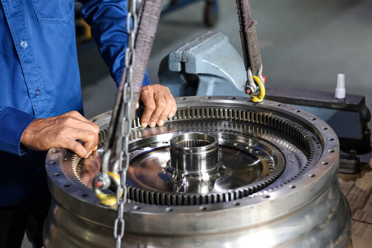 Heavy duty automatic transmission torque converter being lifted by crane with industrial sling in automotive workshop.