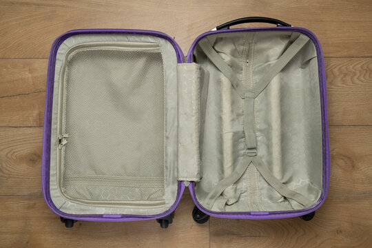 Open empty suitcase on wooden floor ready for travel packing and organization.