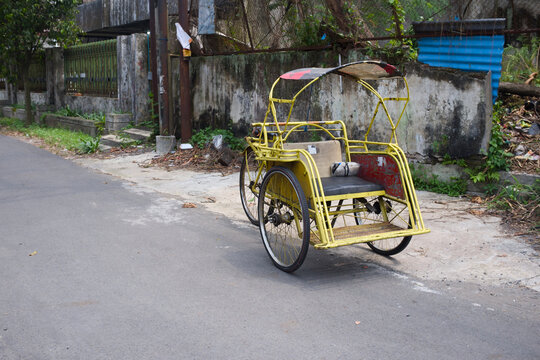 Traditional Yellow Becak Pedicab Parked on Urban Street Side - Authentic Cultural Heritage and Vintage Transport