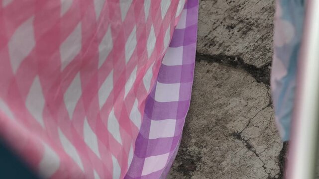Close up of Pink and Purple Gingham Fabric Gently Blowing in the Wind Against a Textured Wall