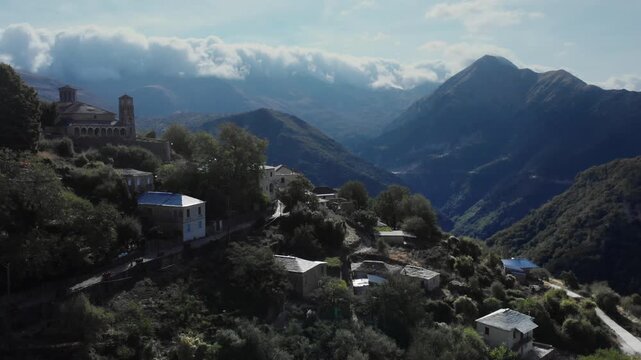 A serene mountain village nestled among lush hills with dramatic cloud-covered peaks. Perfect for tourism ads or travel documentaries.