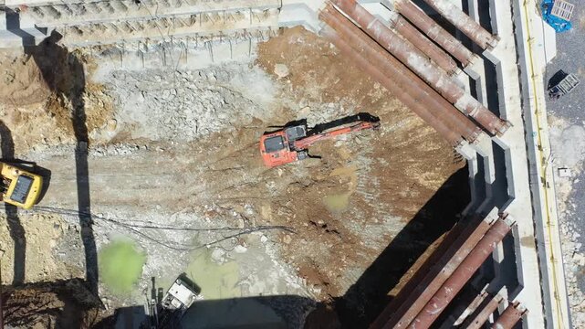 Drone shot of excavator and ground improvement machine working under steel strut pipes in deep foundation excavation. Shoring systems in engineering and heavy industry.