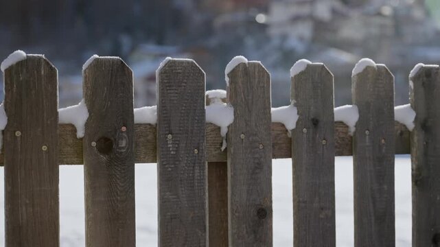 Cold winter outdoor in small town or farm in Europe snow falls on wooden fence. Sunny morning in cold freezing day. Snow storm at night falling on local village or ski resort town. Barrier with snow