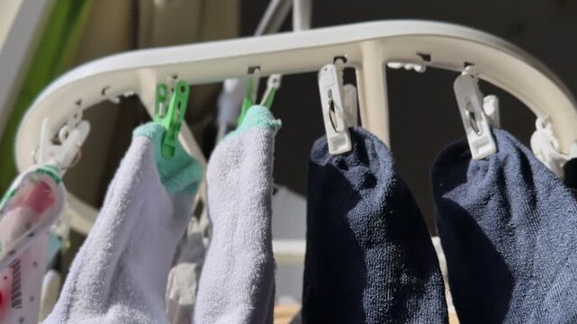 Close-up of infant socks clipped to a white indoor drying rack near a sunny window, highlighting soft textile texture, household washing routine, and cozy daylight home organization.