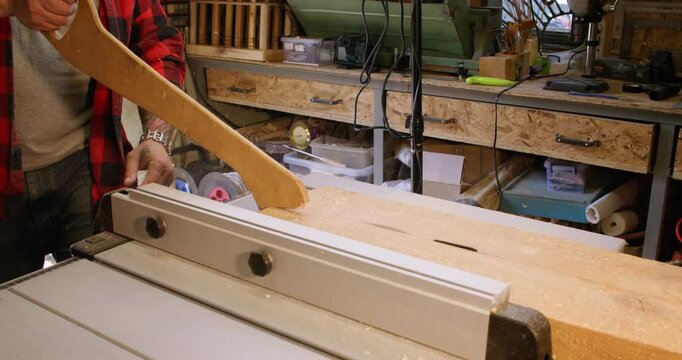 Cutting wood. Workshop safety. Carpenter in plaid shirt dividing plank with circular table saw pushing lumber on rotating sharp blade.