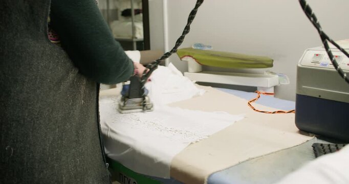 Dressmaking process. Ironer smoothing textile. Woman seamstress steaming white lace fabric with professional appliance in tailor workplace.