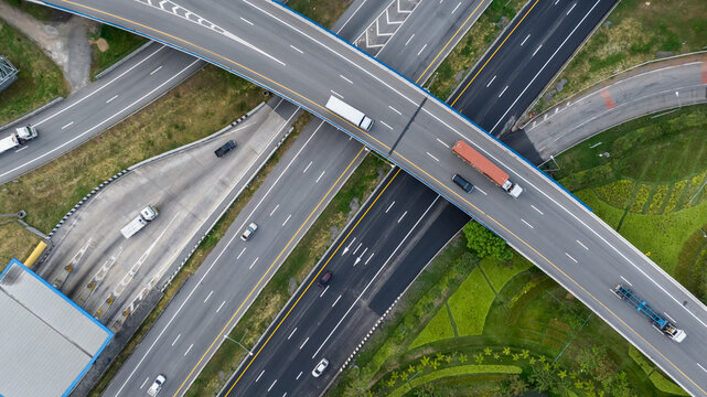 Aerial top view of highway junction interchange road. Drone view of the elevated road, traffic junctions, and green garden. Transport trucks and cars driving on highway. Infrastructure in modern city.
