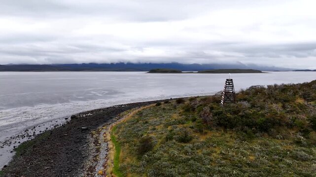 Cinematic orbit circling a red and white striped maritime navigation beacon on the rugged, grassy ridge of Harberton Peninsula in the Beagle Channel