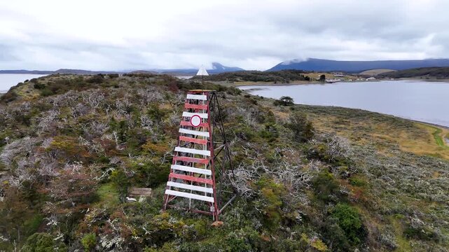 Cinematic orbit circling a red and white striped maritime navigation beacon on the rugged, grassy ridge of Harberton Peninsula in the Beagle Channel