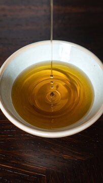 Golden Liquid Pouring into White Bowl Creating Ripples.