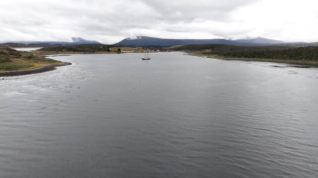 Cinematic flying forward over the calm waters of the Beagle Channel toward the anchored Schooner Amazone in Bahia Harberton, Tierra del Fuego, Argentina