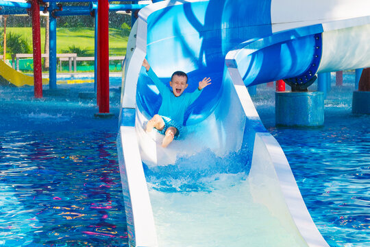 happy funny child boy rides a water slide in a water park in summer vacation. Children's aquapark in swimming pool at the resort