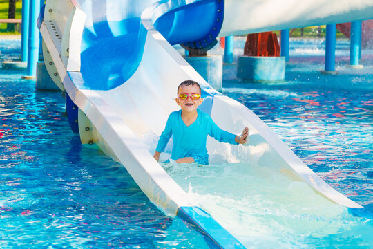 happy cute child boy rides a water slide in a water park in summer vacation. Children's aquapark in swimming pool at the resort