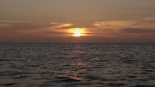 Aerial shot with a drone moving over the sea towards the sun during sunset