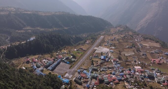 Aerial shot of Lukla Tenzing Hillary Airport set beside a colorful Himalayan village with green forest on rugged terrain and gateway of sagarmatha in the Everest region of Nepal.