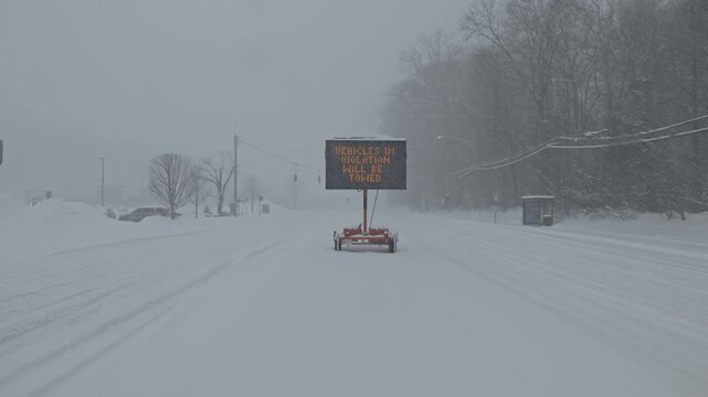 An emergency snow declaration sign on an empty road during a blizzard wide shot