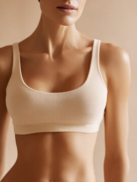 Athleisure and fitness apparel marketing &ndash; cropped woman torso wearing beige sports bra in neutral studio background