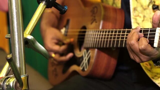 Close-up of a professional South Asian artist strumming an acoustic guitar during a live unplugged session