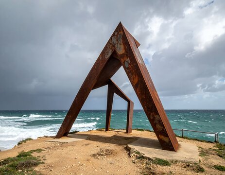 Rusty Metal Sculpture on Coastal Cliff Overlooking Ocean Under Stormy Sky.