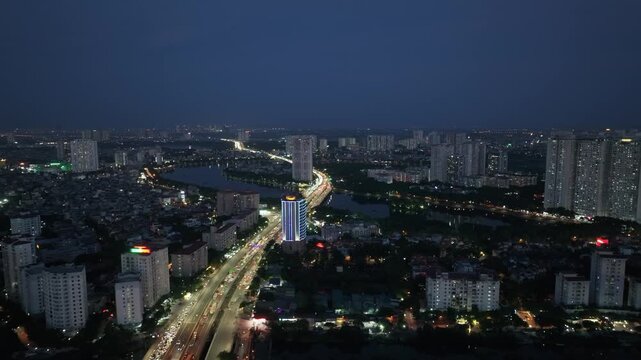 Night aerial view of Ring Road 3 curving past Linh Dam area with illuminated buildings and continuous vehicle flow across dense urban landscape