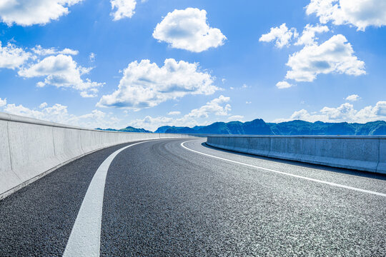 Empty curved asphalt road under a clear blue sky with white clouds