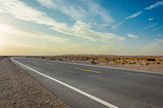 Empty asphalt road stretching through a vast arid desert under a clear blue sky