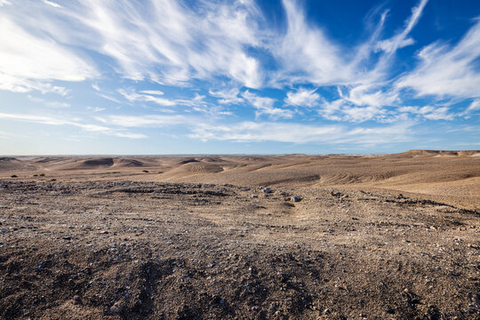 Barren Gobi Desert terrain under dramatic cirrus clouds and a clear blue sky