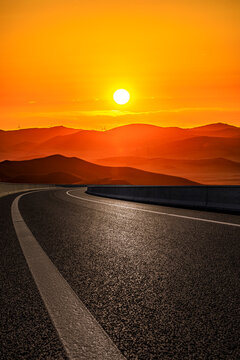 Empty asphalt highway winding towards a majestic mountain range at golden sunset