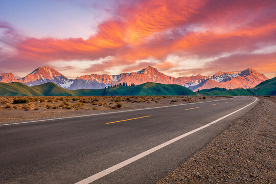 Empty asphalt highway leading towards majestic mountains at sunset. Road trip and travel concept.
