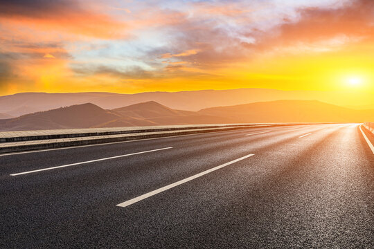 Empty asphalt highway through mountain landscape under dramatic sunset sky. Road trip and travel concept.