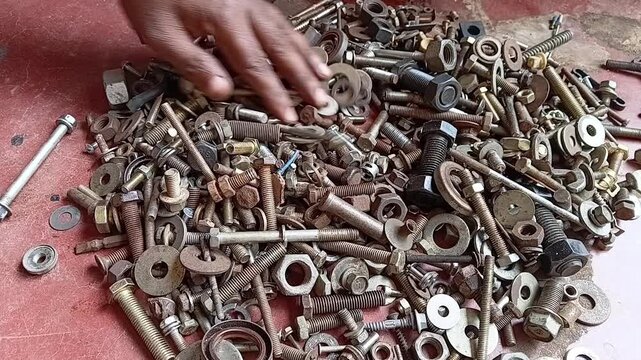 Close up of an oily mechanic hand rummaging and searching through a large messy pile of rusty nuts, bolts, and scrap hardware. Concept of troubleshooting and finding a solution.