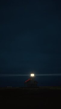 Vertical Screen: Lighthouse tower with bright beam cutting foggy night sky near Mendocino, California, USA creating minimal cinematic coastal night composition