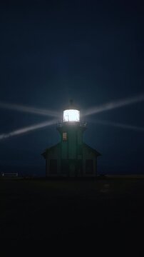 Vertical Screen: Vertical night view of Point Cabrillo Lighthouse with rotating beacon shining through coastal fog above Mendocino, California, USA creating dramatic cinematic atmosphere