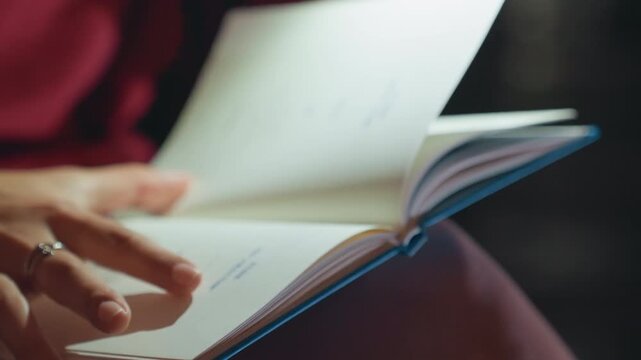 Closeup of person flipping notebook pages hands in red sweater turn bluebound journal slowly, ringed finger pauses on margin, soft warm light and shallow depth of field create cozy reflective mood