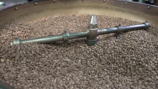 Close-up real shot of coffee beans being roasted in a professional drum roaster. Natural roasting process with rotating mechanism and even heat distribution. Authentic production footage, not AI gener