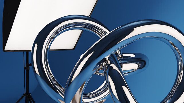 Professional photo studio setup with a reflective chrome 3D abstract knot sculpture on a blue background illuminated by a large white softbox light on a tripod stand