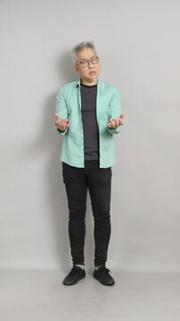 A mature East Asian man showing open hands with a confused and questioning facial expression, looking at the camera as if asking "Why?".