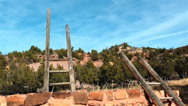 A slow motion orbiting shot captures ancient wooden ladders descending into a sacred stone kiva. This footage highlights the historical architecture and cultural heritage of the ancient site.