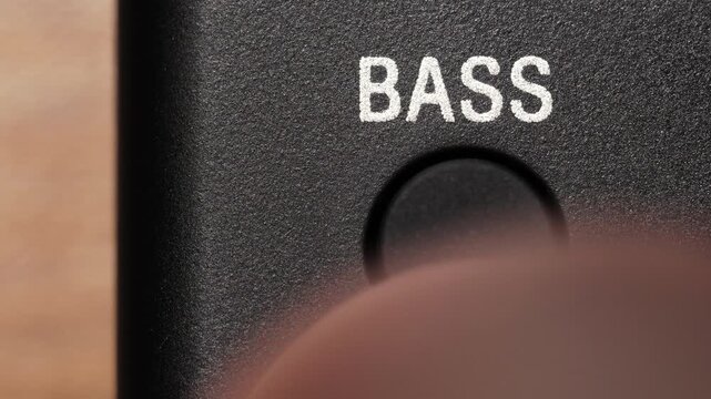 Macro view of finger pressing black bass button below white text on black panel