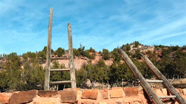This cinematic orbiting view shows traditional kiva ladders at a remote ancient archaeological site. Sunlight highlights the circular stone masonry and weathered wood rungs of the structure.