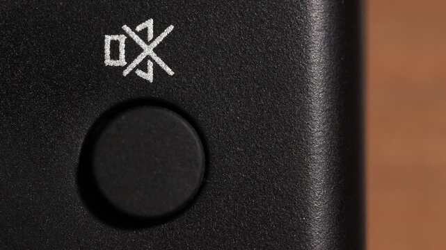 Finger presses black mute button with white audio off icon on black remote