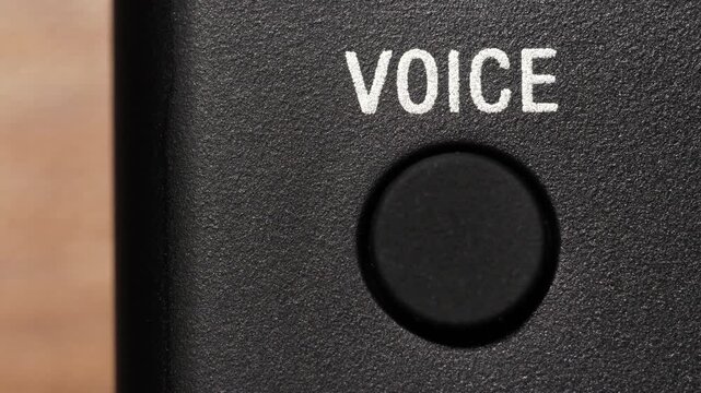 Macro view of finger pressing black voice button below white text on black panel