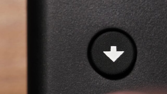 Macro view of finger pressing black down arrow button with white icon on black panel