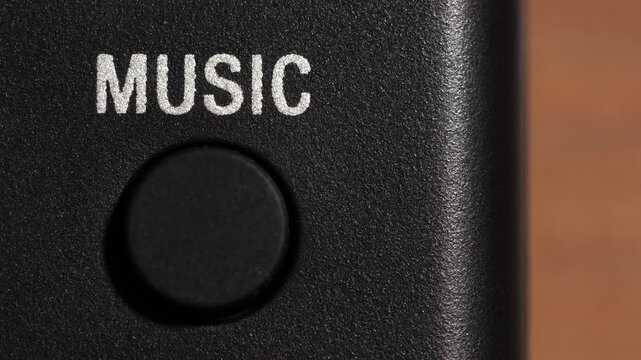 Finger presses black music button beneath white text on black panel